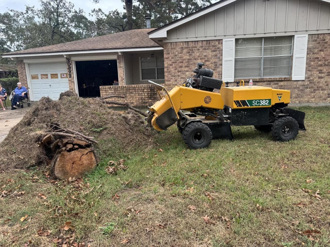 Vermeer stump grinder parked beside a stump and pile of grindings in a residential front yard